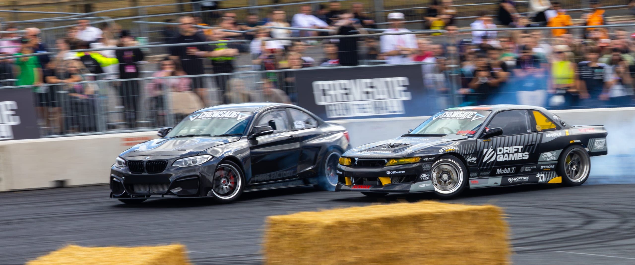 Two drift cars running in close tandem beside the bales, Gravity 2026
