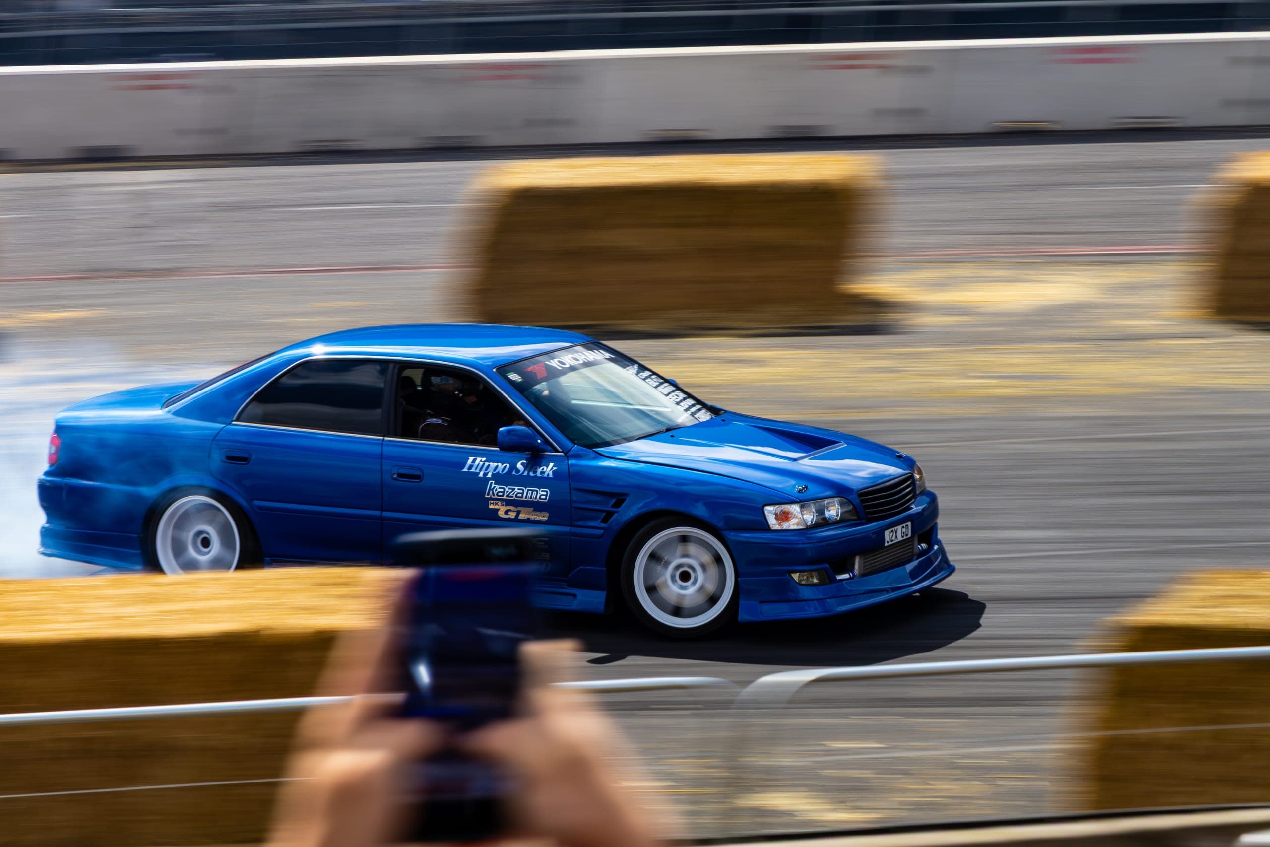 A drift car framed between spectators filming on their phones, Gravity 2026